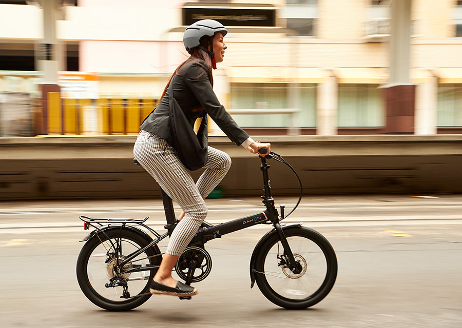 A woman rides a DAHON Unio E20 folding e-bike on a city street, showcasing modern urban mobility with electric assistance.