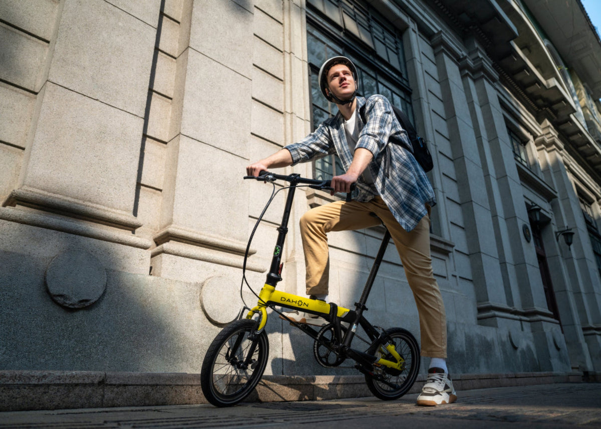 Man riding bright yellow Dahon K-Feather ultra-lightweight e-bike with black accents on city street.